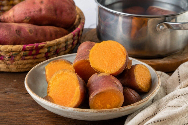 Camote anaranjado hervido en olla con vapor y utensilios de cocina